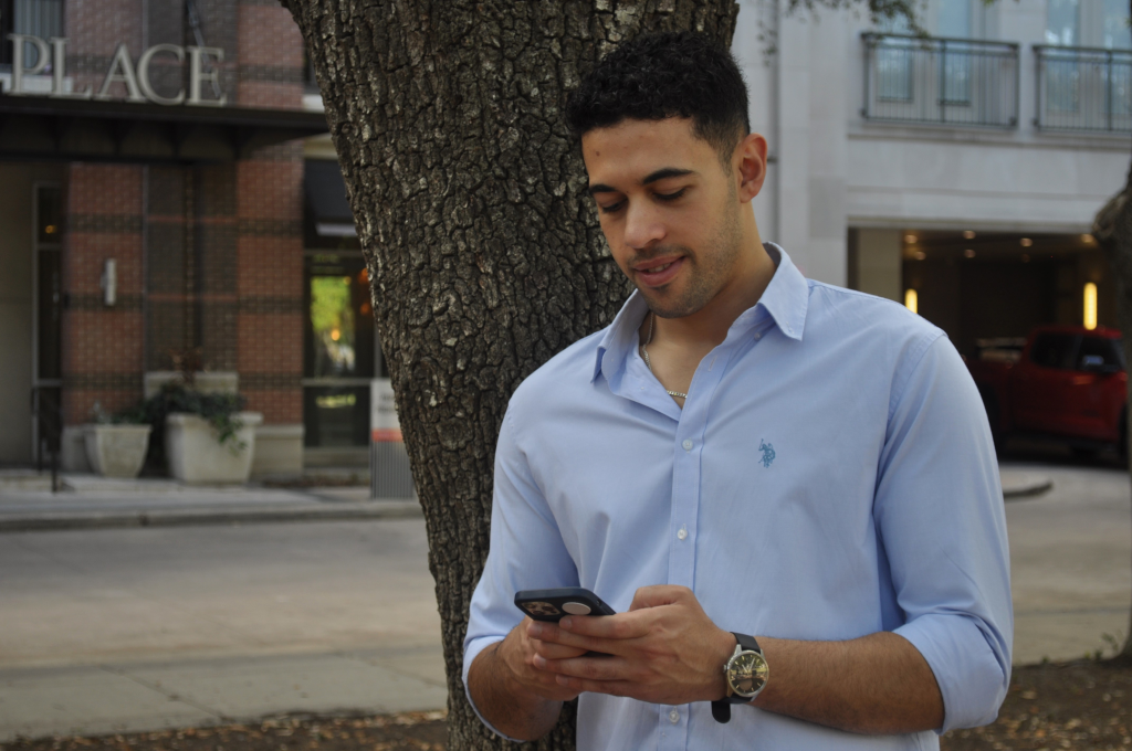 Mahmoud explores his phone with a tree prominently in the background.