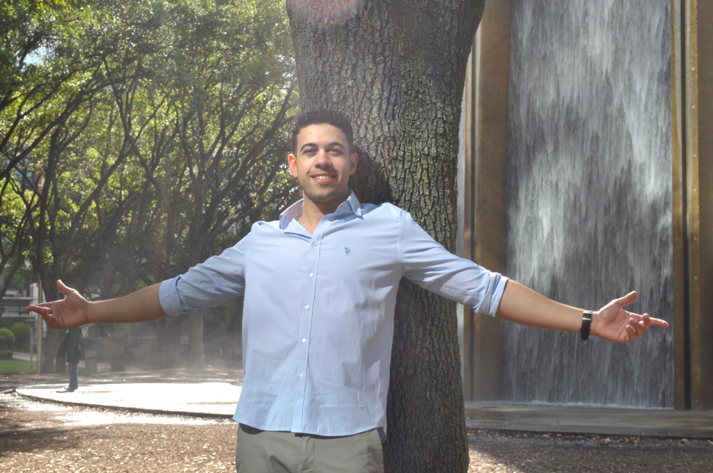 Mahmoud Zaqout leans back against a tree with the Houston Waterwall in the background.